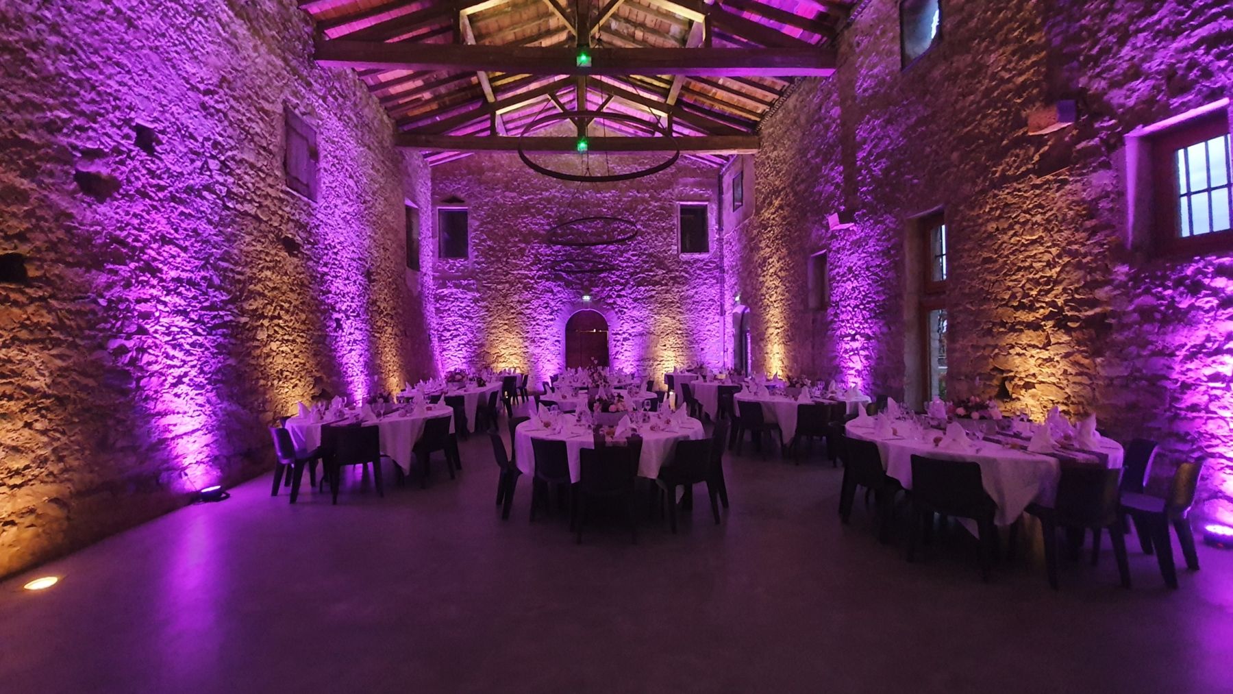 Salle de réception aux murs de pierre mis en lumière, tables dressées